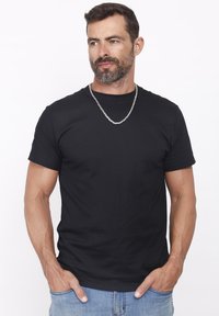 Sort bomulds t-shirt med korte ærmer, rund halsudskæring og glat tekstur. Har et sølvfarvet kæderekke, båret med blå jeans.