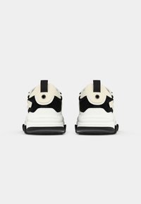 Zapatillas gruesas con una combinación de colores blanco y negro, que cuentan con un exterior de malla texturizada, un collar acolchado y una suela negra gruesa.