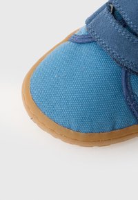 Sinise lõuendjalatsiga, millel on tekstureeritud pind, kummist tallad ja reguleeritav rihm. Ümar varvasetail koos kontrastse õmblusega serva ümber.