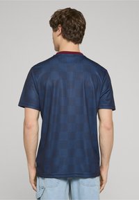 Sötétkék póló kockás mintával, bordó színű kerek nyakkal, rövid ujjakkal, és sima, könnyű anyaggal.