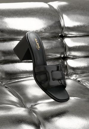 Black heeled sandal with a glossy, smooth finish and wide strap design. Features a block heel and embossed logo on the insole.