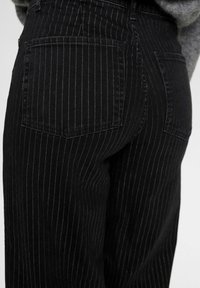 Svarta randiga jeans med hög midja, två bakfickor och en mjuk denimtextur. Ränderna är subtila och jämnt fördelade.
