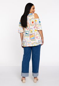 Leichtes, kurzärmliges Top mit Cold-Shoulder-Ausschnitt und buntem, tropischem Muster; kombiniert mit lässigen, umgeschlagenen Jeans und hellen Blockabsatzschuhen.