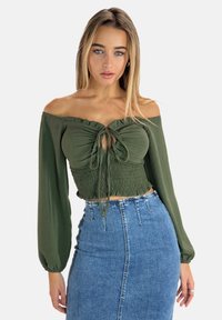 Crop top verde oliva senza spalle con dettagli smock e frontale annodato, abbinato a una gonna a tubino in denim con vita alta.