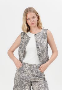 Colete sem mangas em cinza com um padrão de estampado de leopardo. Apresenta botões na parte da frente, combinado com uma blusa branca em canelado e calças a condizer.