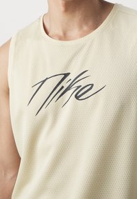 Licht beige mouwloze mesh tanktop met een ronde hals, met een opvallend zwart Nike-logo op de voorkant.