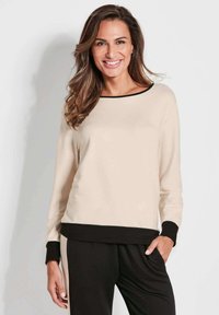 Maglietta beige a maniche lunghe con bordo e polsini neri, caratterizzata da una vestibilità ampia e una texture morbida, abbinata a pantaloni neri. Design semplice e moderno.