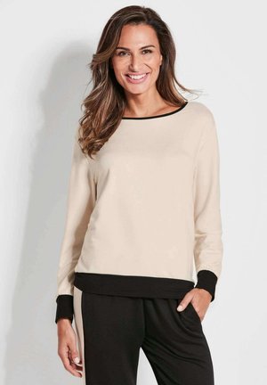 Beige Langarmoberteil mit schwarzem Besatz und Bündchen, für einen lockeren Sitz und weiche Textur, kombiniert mit schwarzen Hosen. Einfaches und modernes Design.