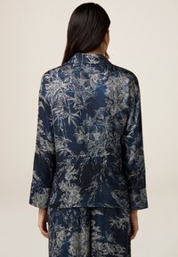 Blouse en soie bleu marine foncé avec imprimé floral argenté. Dotée d'un col cranté et de manches longues, avec une texture lisse et brillante.