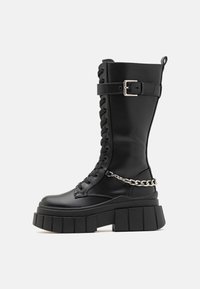 Μαύρο μπότες μέχρι το γόνατο από απαλό υλικό, με χοντρή πλατφόρμα, κορδόνια στο μπροστινό μέρος, λωρίδα με αυτόματο κούμπωμα και αλυσίδα ως διακοσμητικό στοιχείο.