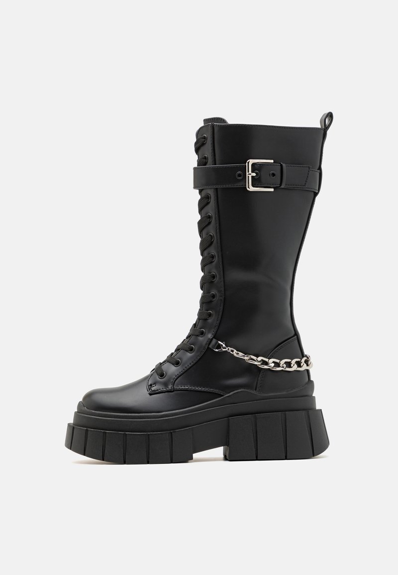 Μαύρο μπότες μέχρι το γόνατο από απαλό υλικό, με χοντρή πλατφόρμα, κορδόνια στο μπροστινό μέρος, λωρίδα με αυτόματο κούμπωμα και αλυσίδα ως διακοσμητικό στοιχείο.