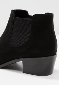 Schwarze Wildleder-Ankle-Boots mit einem strukturierten elastischen seitlichen Einsatz, einem Gummimidabsatz und einer glatten, abgerundeten Spitze.