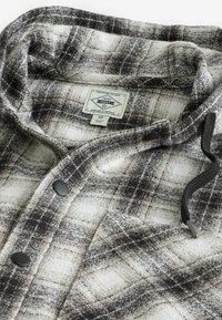 Karierte Flanellhemd in Grau und Weiß, mit weichem Stoff, schwarzen Knöpfen und einem Zugband mit metallischer Spitze. Größe M-Label sichtbar.