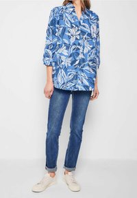Blue floral patterned shirt in lightweight fabric, featuring a v-neck and three-quarter sleeves, paired with rolled cuff jeans and light sneakers.