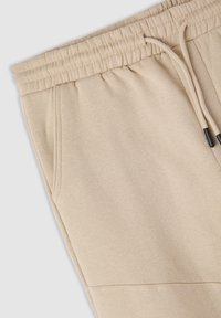 Beżowe dresy z bawełny z elastycznym pasem, detale ze sznurkiem i bocznymi kieszeniami; miękka tekstura i przeszycia dla większej trwałości.