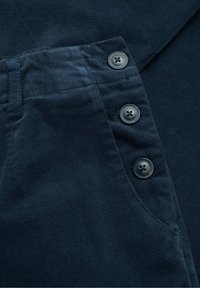 Tumši jūras spēka krāsas audums ar teksturētu virsmu, ar sānu kabatu un trim melnajām pogām. Audums šķiet mīksts un ribots.