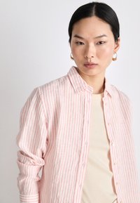 Lightweight, pink and white striped long-sleeve shirt with a button-down front, rolled sleeves, and a soft, textured fabric.
