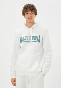 Biała bluza z kapturem, wykonana z miękkiego materiału, z turkusowym nadrukiem "CALIFORNIA Athletic Department." Posiada kieszeń z przodu i sznurki do regulacji kaptura.
