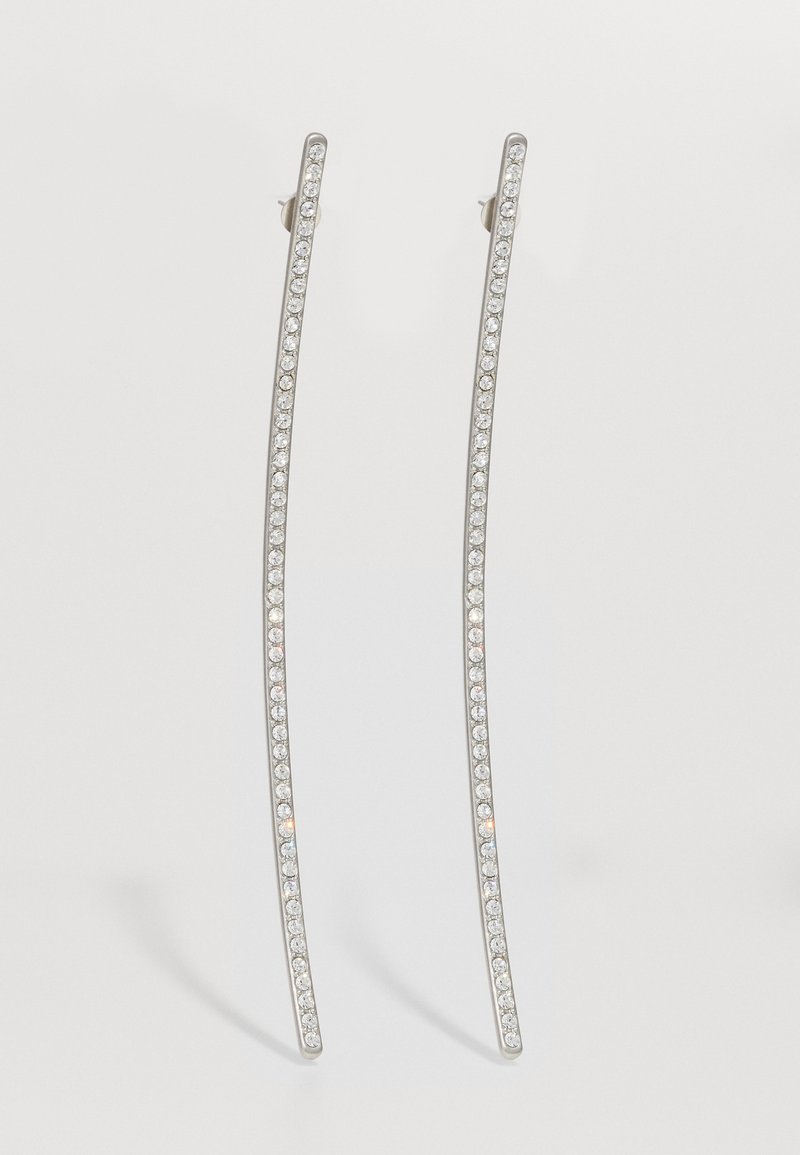 Sudraba tonis, garas auskaru auskaru ar izliekta dizainu, kas rotātas ar skaidru kristālu rindu gar ārējām malām, lai pievienotu papildu mirdzumu.