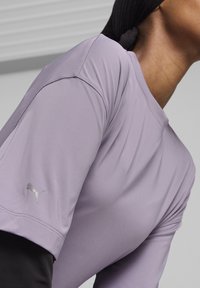 Šviesiai purpurinė sportinė marškinėliai su trumpomis rankovėmis, lygia tekstūra, liekna siluetas, su sidabru Puma logotipu ant kairės rankovės.