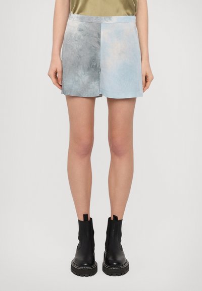 Shorts en denim avec un design bicolore, présentant un côté gris et un côté bleu clair, associés à des bottines noires à la cheville et un haut vert.