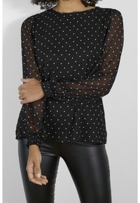Blouse noire à pois blancs en tissu léger et transparent, avec de longues manches bouffantes à poignets élastiques et une coupe décontractée.