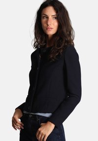 Giacca corta navy con finitura texturizzata, scollatura rotonda, chiusura con un bottone e due tasche frontali, abbinata a una maglietta a righe.