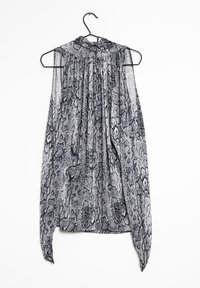 Ärm- och mönstrad blus i svart och vitt med hög krage och veckad design, hängande på en svart krok mot en vit bakgrund.