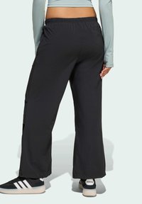 Black athletic pants with a relaxed fit, elastic waistband, and side pockets, paired with black shoes featuring white stripes.