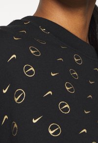 Svart sweatshirt med guld Nike-logotyper och cirkulära mönster. Har rund halsringning och strukturerad tyg.