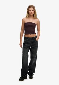 Top sin tirantes, ajustado en rojo oscuro con finas rayas horizontales; combinado con jeans de mezclilla negros y sueltos; el modelo lleva zapatos negros.