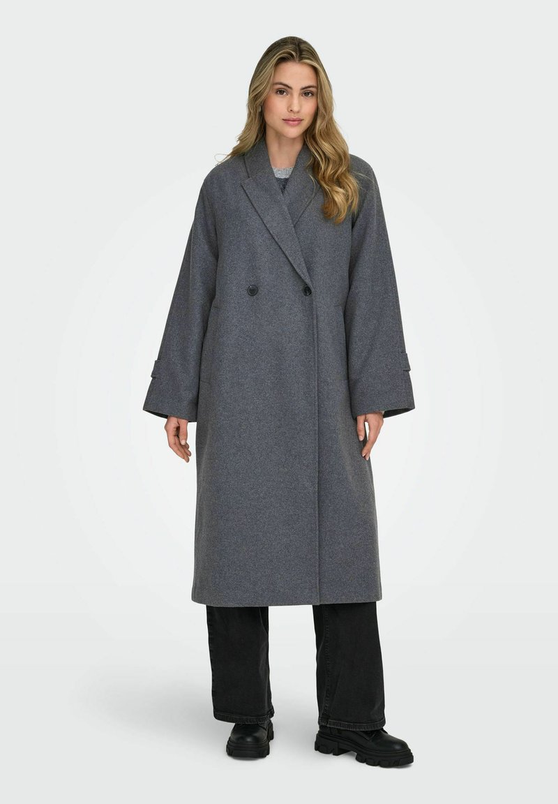 Gray woolen long coat featuring a double-breasted design, wide sleeves, and side pockets. Worn over black pants and chunky black boots.