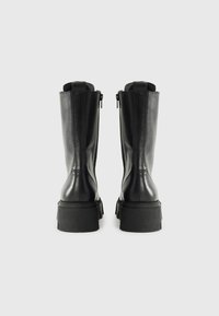 Botas de cuero negras hasta el tobillo con suela gruesa, cremalleras laterales y diseño minimalista. Textura suave y cobertura alta.