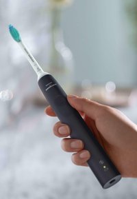 Spazzolino elettrico nero con testina bianca, setole verdi e blu, pulsante di accensione e design ergonomico slim.
