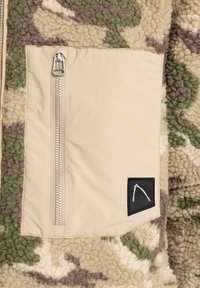 Beige ritszak op een gestructureerde fleece jacket met een camouflagepatroon in groen, bruin en crème. Zwarte logo-label aanwezig.