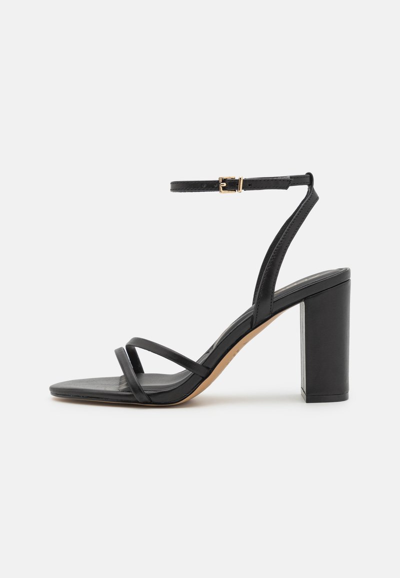 Must musta kõrge kontsaga sandaal, millel on ruudukujuline varvas, kaks kitsast rihma jala peal ning ankle strap, mis on varustatud kuldse pandlaga.