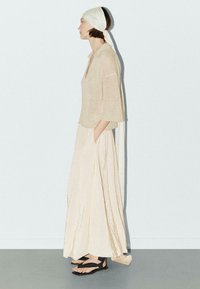 Beige gebreide top met 3/4 mouwen, keyhole halslijn; vloeiende crèmekleurige rok; zwarte sandalen met banden; gladde textuur; minimalistisch ontwerp.