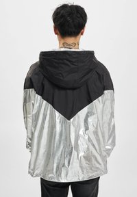 Kapuzenshirt mit einem schwarzen oberen Bereich und einem reflektierenden silbernen unteren Bereich, mit einem Chevron-Muster und glatter Textur.