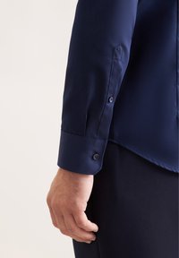 Donkerblauwe langemouwen shirt met een gladde textuur, voorzien van een knoopmanschette en subtiele logodetails op de mouw.