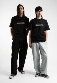 Svarte bomulls t-skjorter med "WASTED" grafikk i hvitt. En modell har på seg svarte bukser, den andre grå joggebukser. Begge har på seg svarte sneakers.