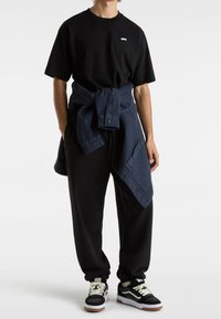 Černé bavlněné tričko s malým logem, volné tmavě modré kalhoty a černé tenisky s krémovými tkaničkami. Texturovaná košile uvázaná kolem pasu.