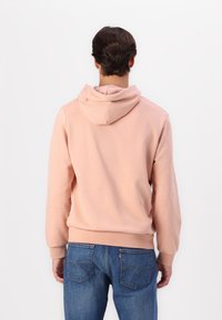 Sudadera rosa claro con capucha ajustable, puños y dobladillo acanalados. Combinada con jeans de denim azul, mostrando un corte relajado y una textura suave.
