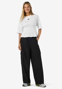 Balti trumpu rankoviu marškiniai su rauktu liemeniu ir logotipu, derinami su plačiomis juodomis kargo kelnėmis, turinčiomis šonines kišenes ir elastingą juosmenį.