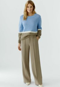 Hellblauer Strickpullover mit breitem weißen und braunem Streifen, kombiniert mit hoch taillierter beiger Hose mit maßgeschneiderten Falten.