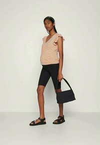 Top envolvente riscado em laranja e branco, com mangas largas, combinado com calções ciclista pretos e uma bolsa preta. Usado com sandálias pretas com tiras.