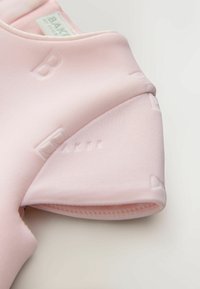 Jasnoróżowy strój z krótkim rękawem, ozdobiony wypukłymi literami na tkaninie, o gładkiej fakturze i okrągłym dekolcie.