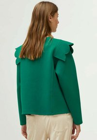 Sudadera verde con cuello redondeado y detalles en los hombros con borde, fabricada en un tejido suave, con mangas largas y un corte holgado.