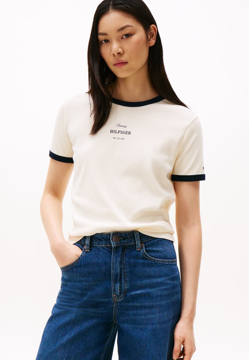 Hvid kortærmet T-shirt med marineblå kontrast i kraven og ærmerne. Har "Tommy HILFIGER" logoet trykt i marineblå. Bæres med højtaljede denimjeans.