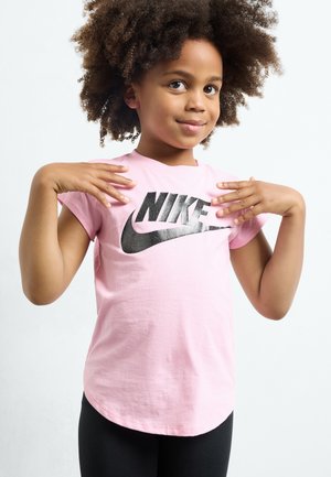 Roosa puuvillane T-särk lühikeste varrukatega, kus on üle rinna suur must Nike logo. Mudel kannab musti legginsi, näidates lõdva stiili.