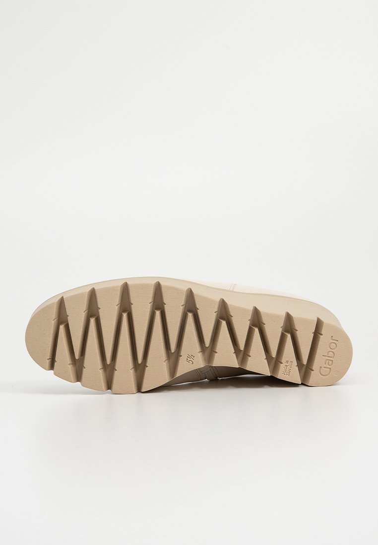 Beige instapschoen met een gestructureerde rubberen zool, voorzien van een zigzagpatroon voor grip en een gladde bovenkant. Logo zichtbaar aan de zijkant.